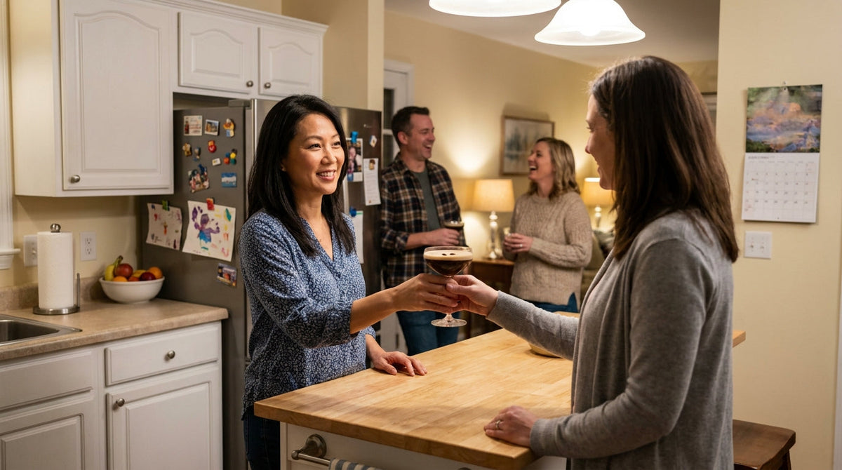 A woman handing a freshly made espresso martini to a friend at a relaxed get-together in her home kitchen.