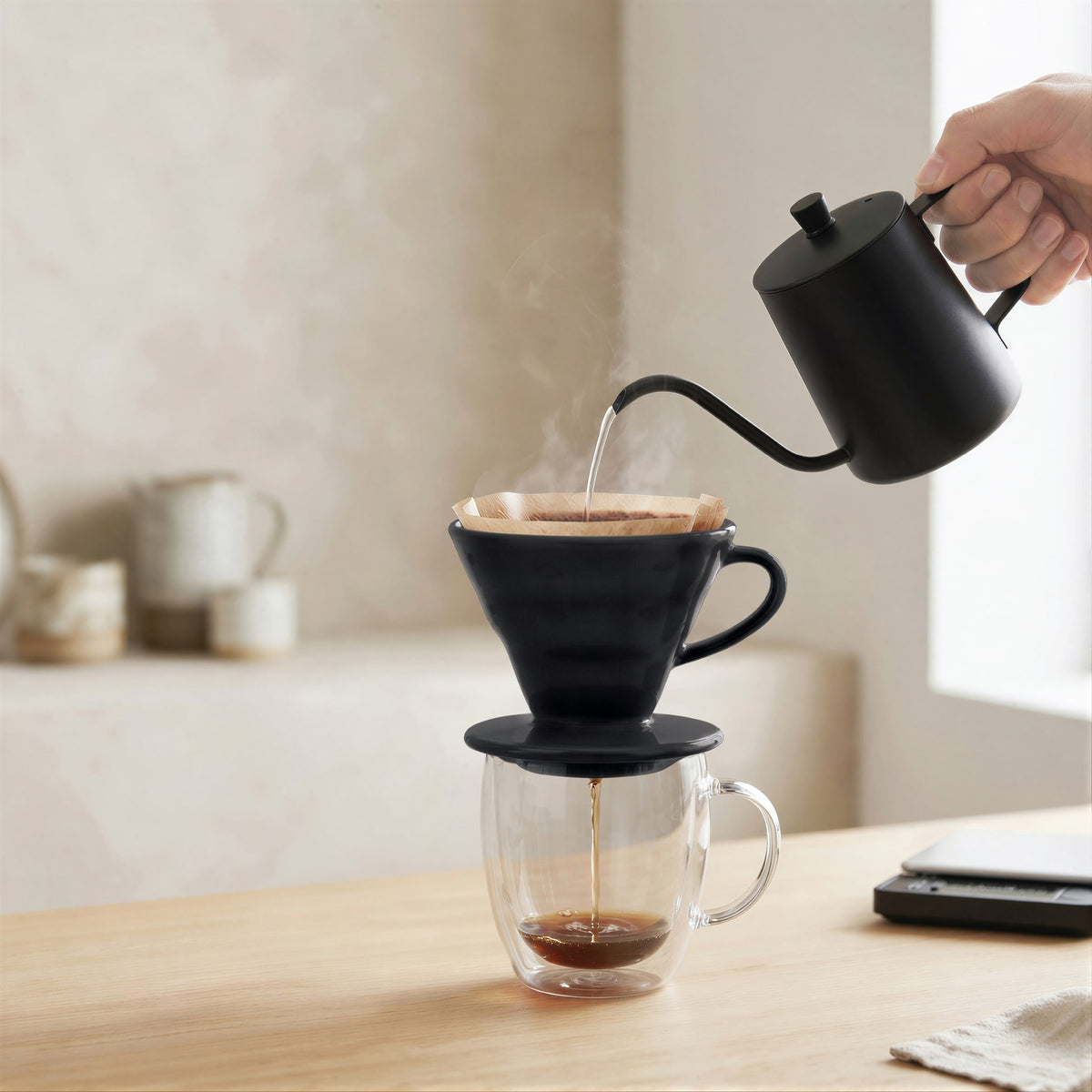 Pouring hot water from a gooseneck kettle into the black pour over dripper on a kitchen counter